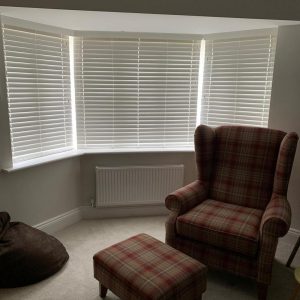 white faux wood Venetian blinds in living room with armchair