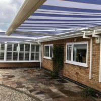 Blue and white striped electric awnings from a side angle on rear of property roof