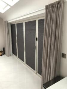 grey duette blinds on french doors with brown curtains on either side.