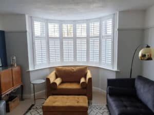 an image showing a brightly lit window with window shutters behind a bright yellow armchair.